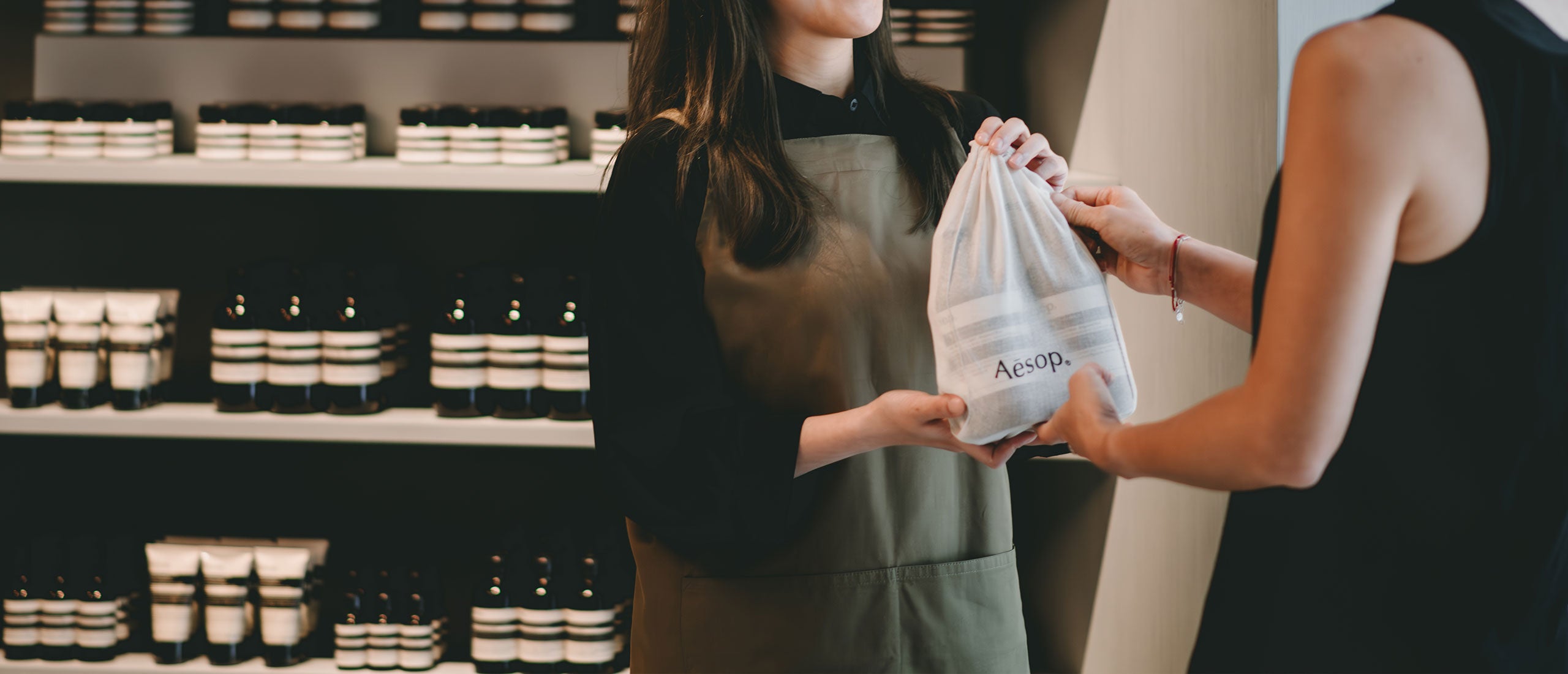 An Aesop consultant hands our signature cotton bag filled with products to a customer.
