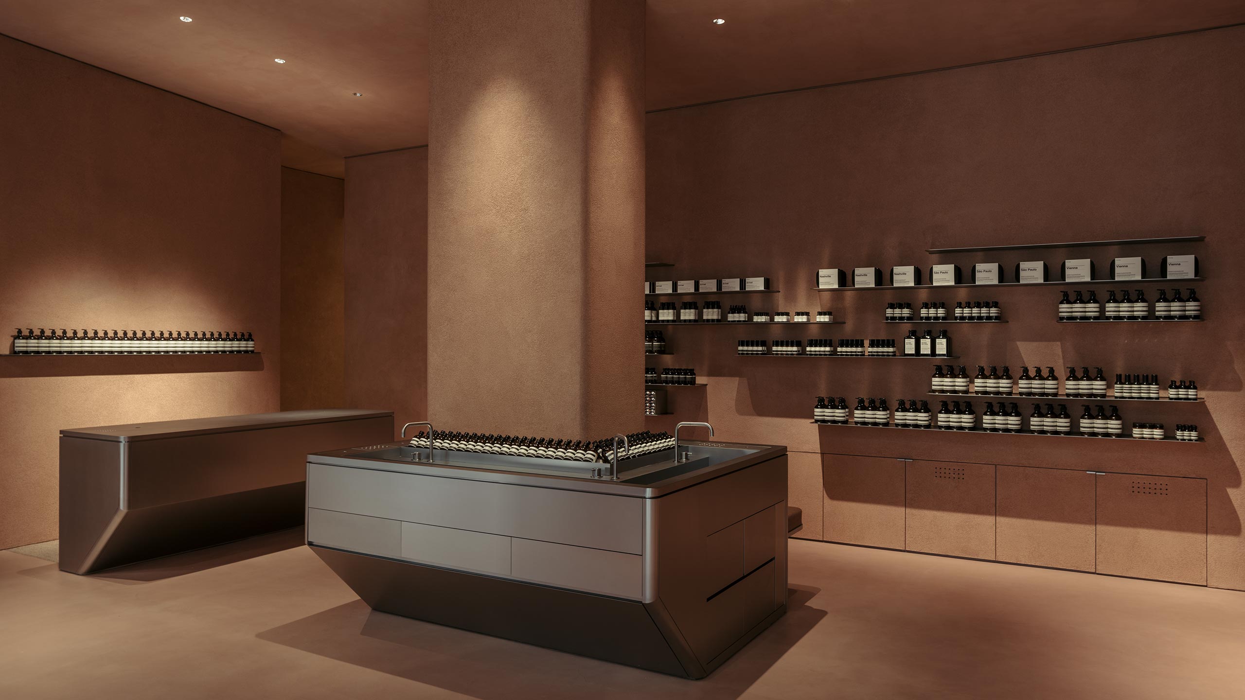 The interior is evocative of natural clay with the walls and central pillar coloured in  natural terracotta tones. There is a stainless-steel basin below the pillar.