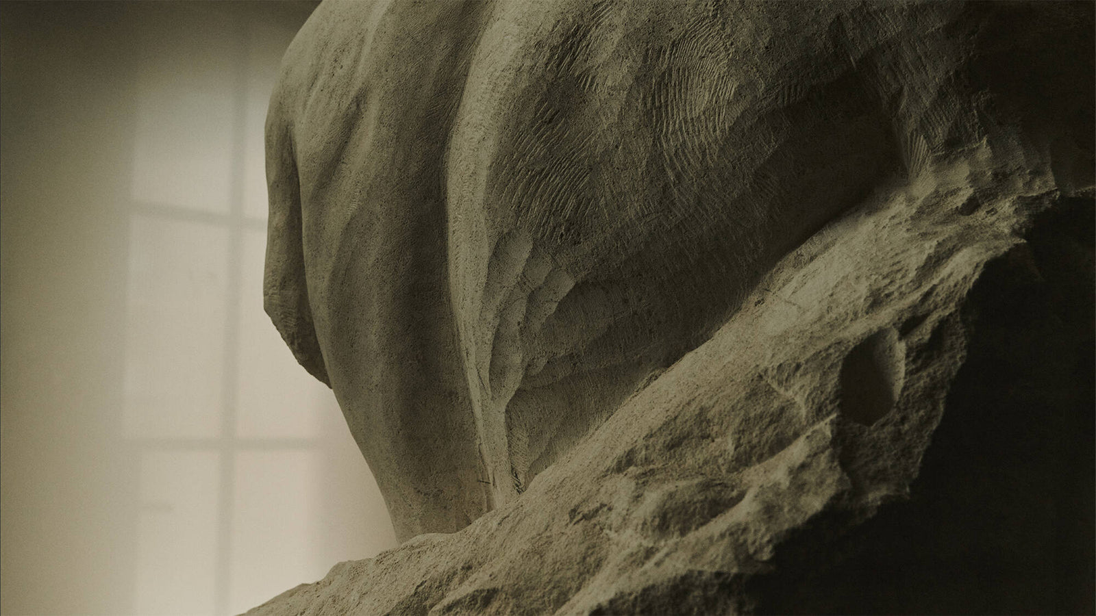 Close-up of a rough stone sculpture with soft window light in the background.
