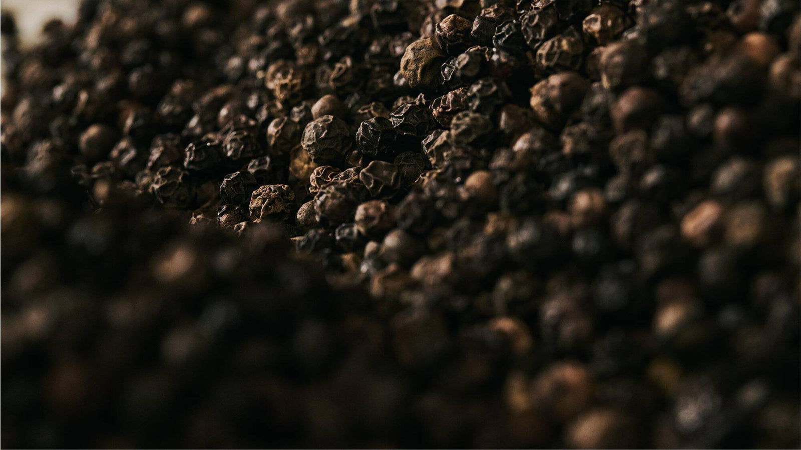 Close-up of black peppercorns scattered across a dark textured surface.